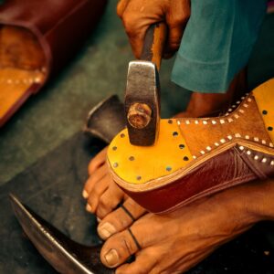 Close-up of a shoemaker handcrafting leather shoes with a hammer.